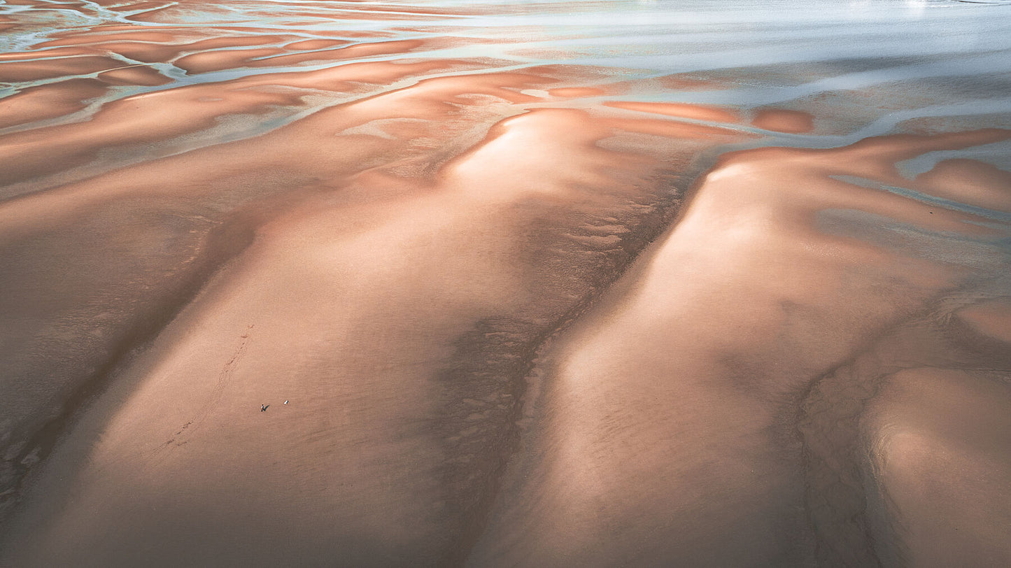 Man with the dog on a desert like beach on tide out, Wales. Print or framed photography art.